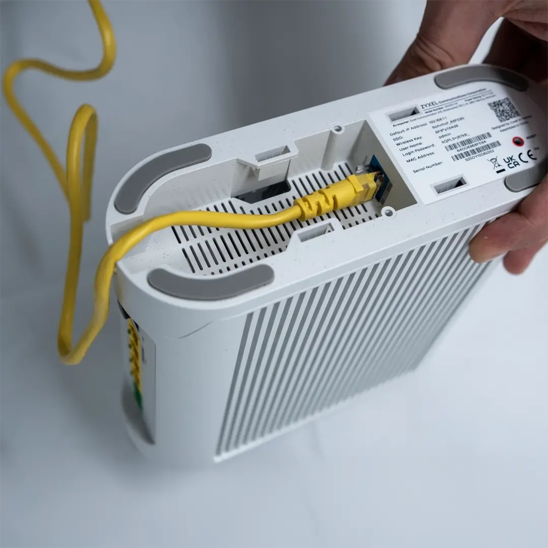 En person holder en Zyxel-ruter og har koblet en gul nettverkskabel til porten på undersiden av enheten.