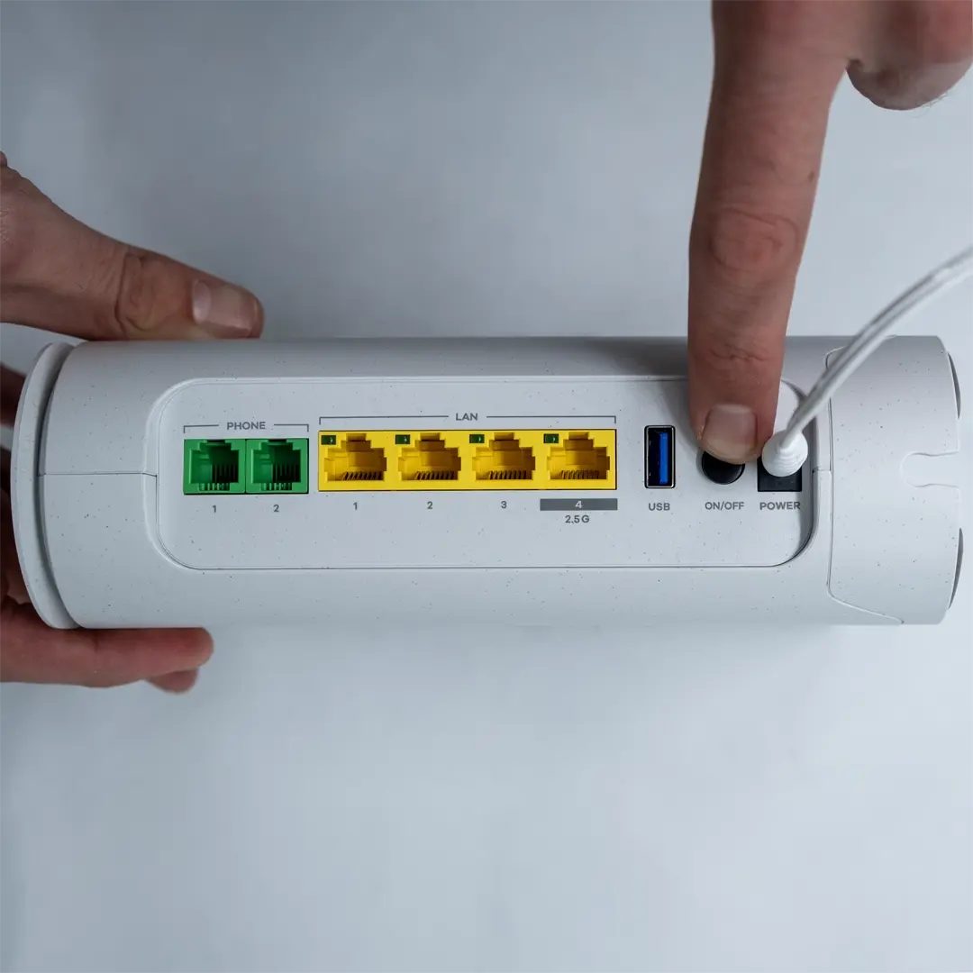 En person trykker på av/på-knappen på baksiden av en Zyxel-ruter for å starte den. Strømkabelen er koblet til, og de gule LAN-portene samt USB-porten er tydelig synlige.