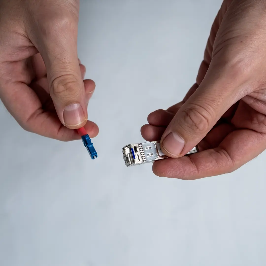 En person holder SFP-modulen i den ene hånden og viser kontakten på den blå fiberkabelen i den andre.