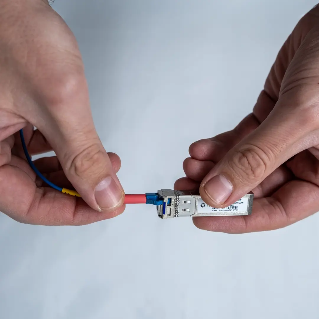 En person kobler den blå fiberkabelen til SFP-modulen ved å føre kontakten forsiktig inn til den klikker på plass.
