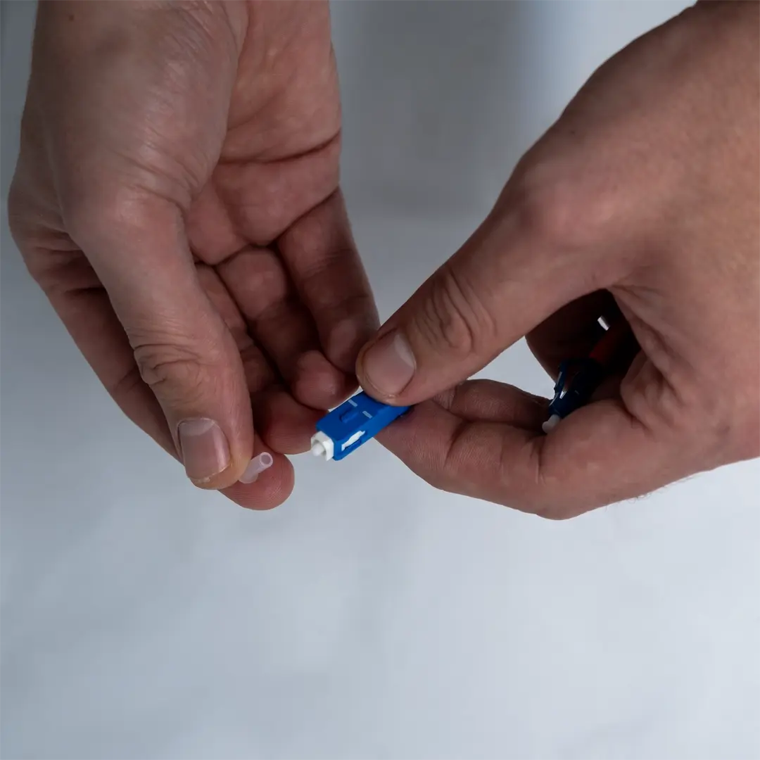 En person fjerner den gjennomsiktige beskyttelseshetten fra enden av den blå fiberkabelen.
