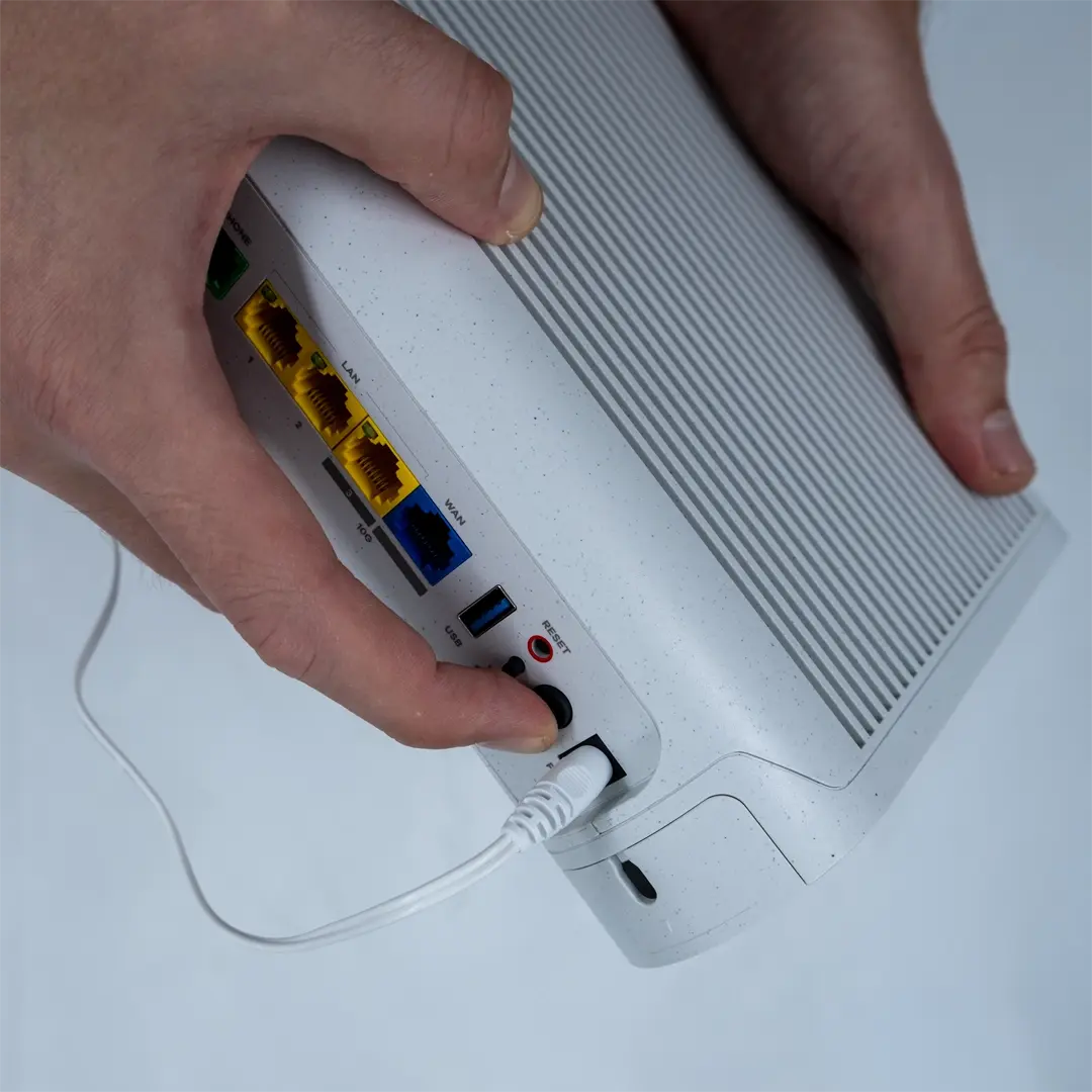 En person trykker på av/på-knappen bak på ruteren etter at strømkabelen er koblet til stikkontakten.