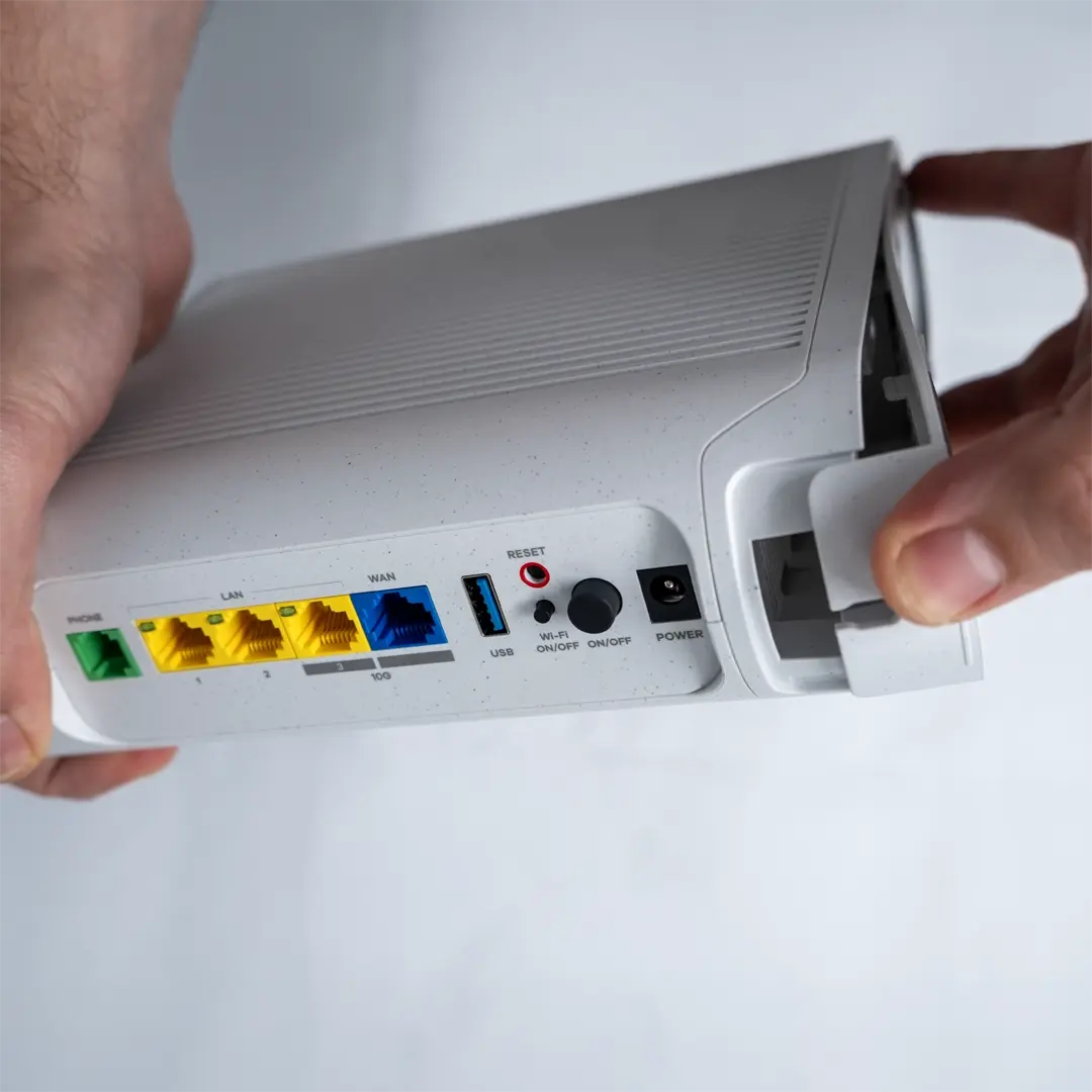 En person fjerner forsiktig bunnpanelet på ruteren ved å trekke i kanten.