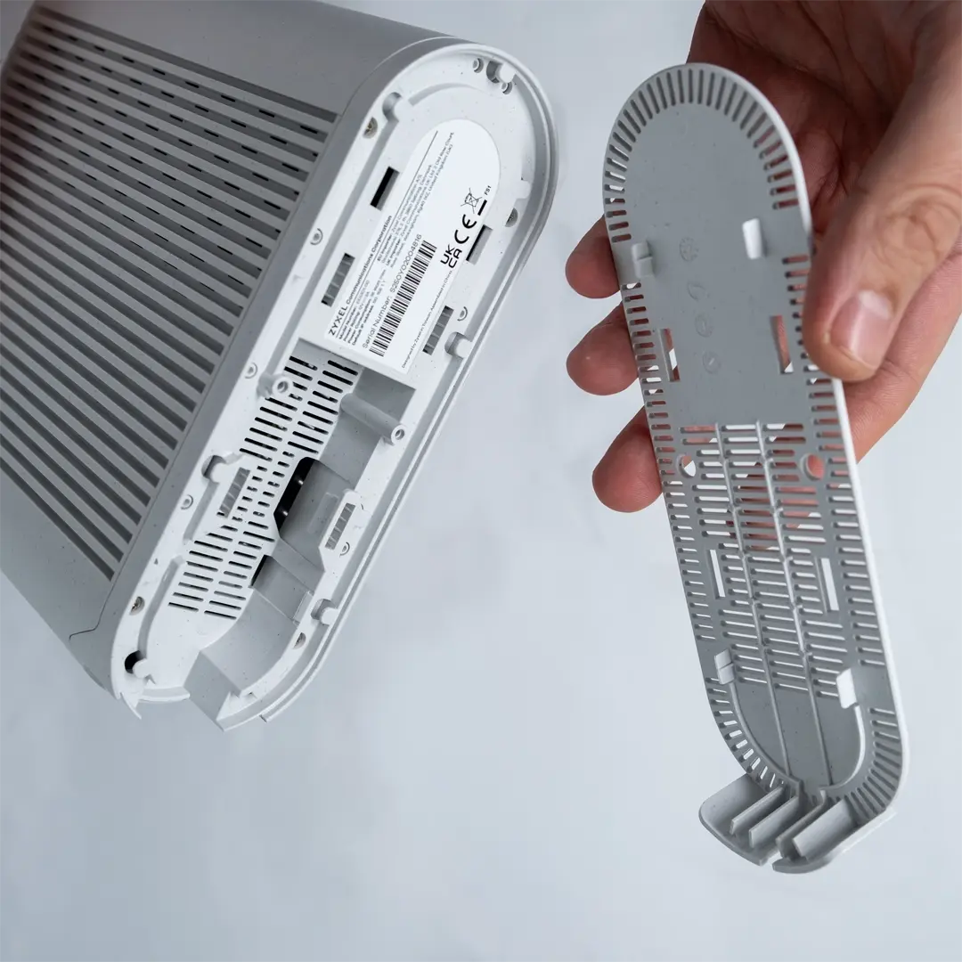 En person har tatt av bunnpanelet og holder det ved siden av enheten slik at kontaktene på undersiden av ruteren er synlige.