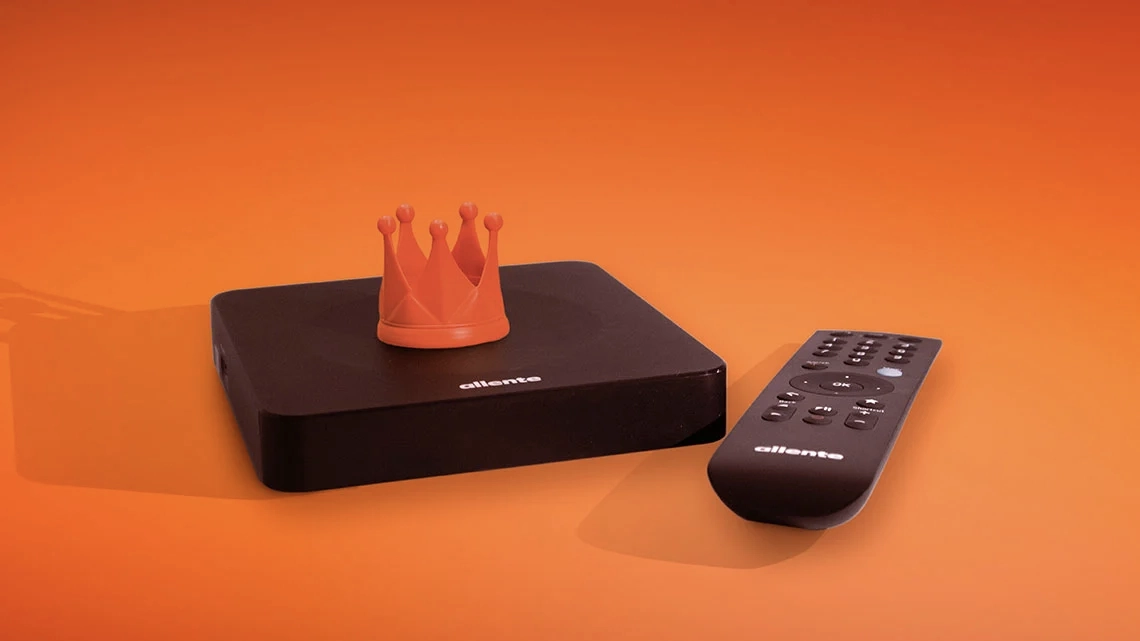 En svart TV-boks fra Allente med en fjernkontroll ved siden av, plassert mot en oransje bakgrunn.